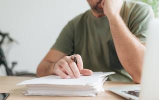 Eine Person prüft am Schreibtisch handschriftlich ihre Notenübersicht und notiert offene ECTS Punkte für die schriftliche Anfrage beim Prüfungsamt
