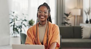 Junge Frau lächelt am Laptop zu Hause, Weiterbildung Entrepreneurship im Sozialmanagement